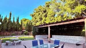 Eine Terrasse im Freien mit einem Glastisch und Stühlen, umgeben von einer Steinpatio und einer Holzpergola.