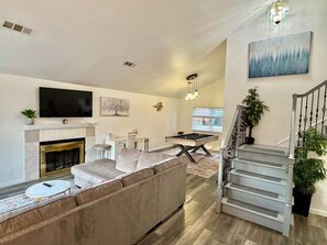 A living room with a fireplace, a pool table, a sofa, and a staircase.