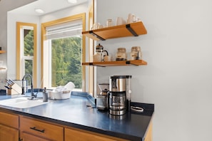 Eine moderne Küche mit schwarzer Arbeitsplatte, Holzschränken, einer Kaffeemaschine und einem Fenster mit Blick ins Grüne.