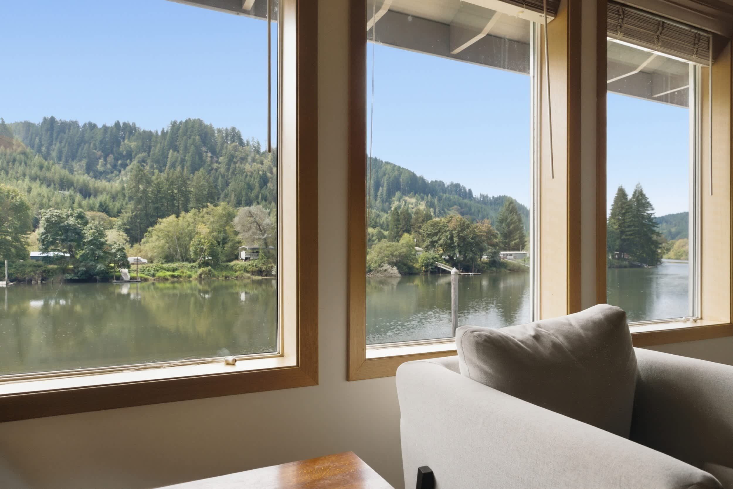 A room with a view of a lake and forest, a sofa, and a table.