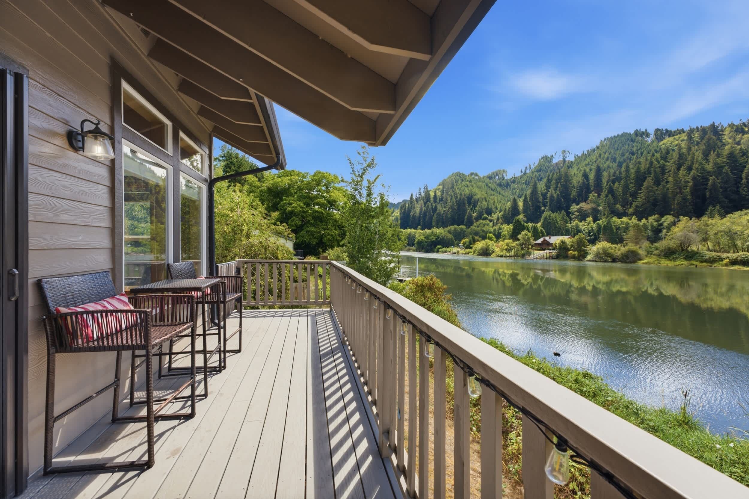 A wooden deck with outdoor furniture, overlooking a calm lake and forested hills.