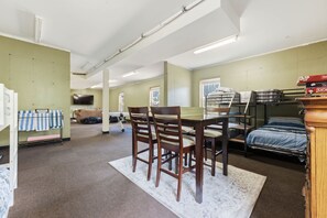 Ein Zimmer mit Etagenbetten, einem Esstisch mit Stühlen, einem Fernseher und einem Fenster.