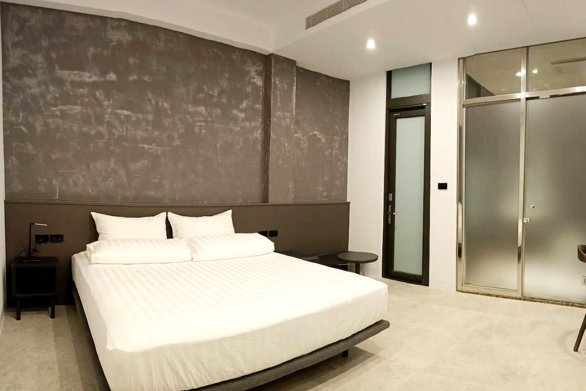 A modern bedroom with a large bed, a nightstand, a small table, and a walk-in closet.