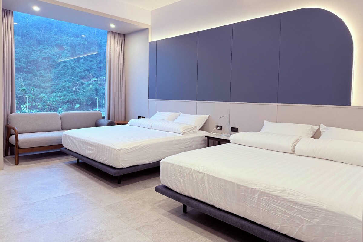 A hotel room with two beds, a sofa, a large window with curtains, and a modern ceiling design.