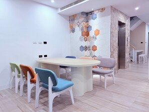 A modern dining area with a round table and white chairs, a hexagonal patterned wall, and a staircase leading to an upper level. - Xingwan (Kaohsiung City)