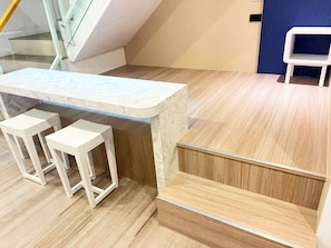 Zona de bar con encimera de mármol y dos taburetes blancos.