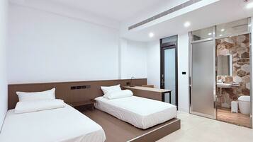 A modern hotel room with two beds, a desk, and a bathroom visible through a glass door.