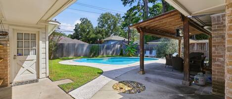 Un jardin avec une piscine, un patio couvert et un mur en briques.