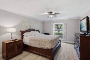 Ein Schlafzimmer mit einem Bett, einem Nachttisch, einer Kommode, einem Deckenventilator und einem Fenster mit Jalousien.