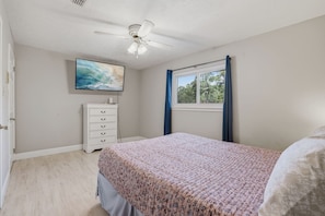 A bedroom with a bed, a dresser, a ceiling fan, a window with curtains, and a painting on the wall. - 5BD North Houston Home | Pool | Table Tennis (Houston)