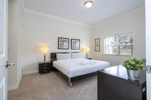 Una habitación de hotel con cama, mesitas de noche, un escritorio, una ventana con persianas y una planta en maceta.