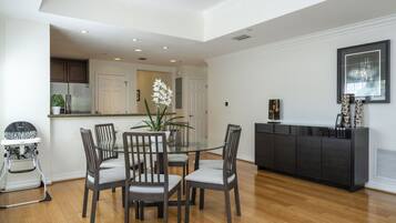 Comedor con mesa de vidrio rodeada de sillas, cocina al fondo y una consola negra con objetos decorativos.