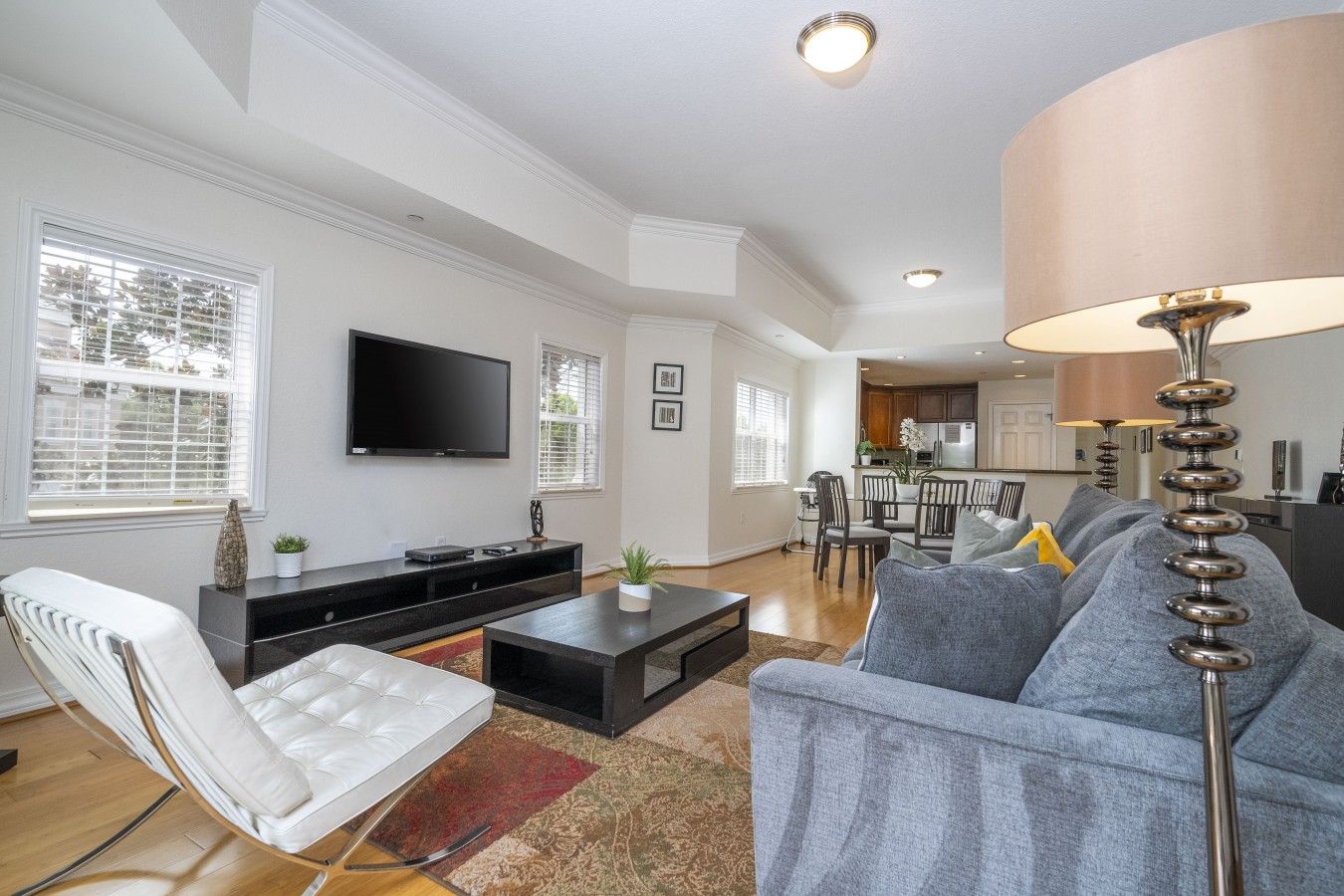 A modern living room with a flat-screen TV, a sofa, a coffee table, and a dining area with chairs and a table.