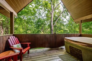 Eine Holzterrasse mit Whirlpool, roten Adirondack-Stühlen und Blick auf einen Wald.
