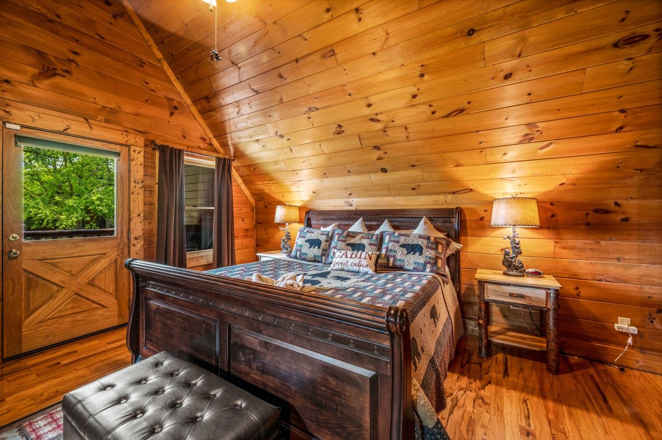 Une chambre dans une cabane en bois, avec un lit, une table de chevet, une lampe, un banc et une fenêtre donnant sur la forêt.