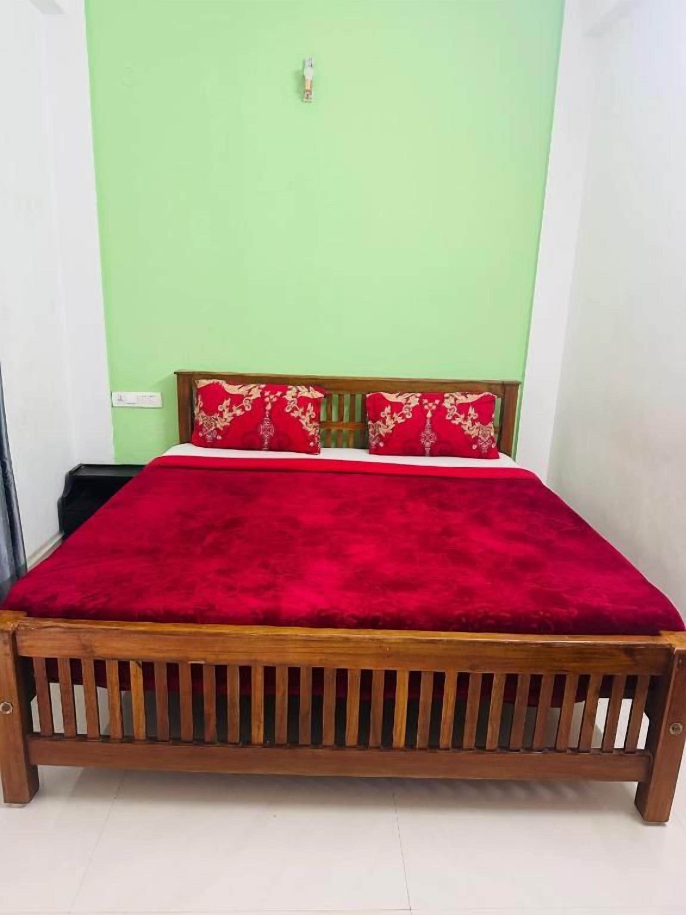 A bed with a red blanket and wooden headboard in a room with green walls.