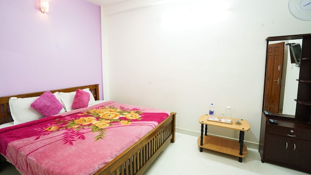 A bedroom with a bed, a wooden bedside table, a mirror, and a wall-mounted light fixture.