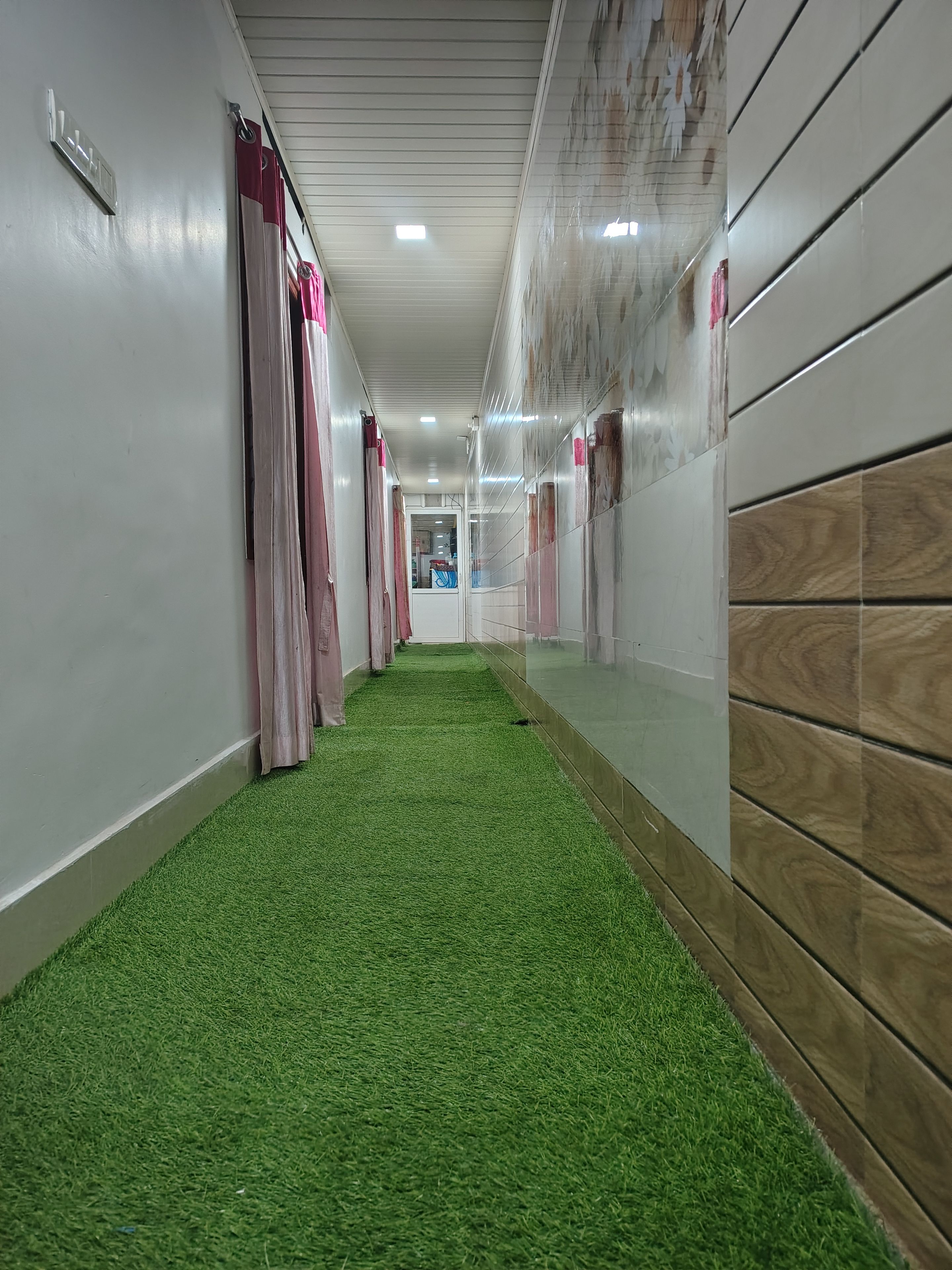 Un pasillo con alfombra verde sintética, paredes blancas y un detalle decorativo de paneles de madera.