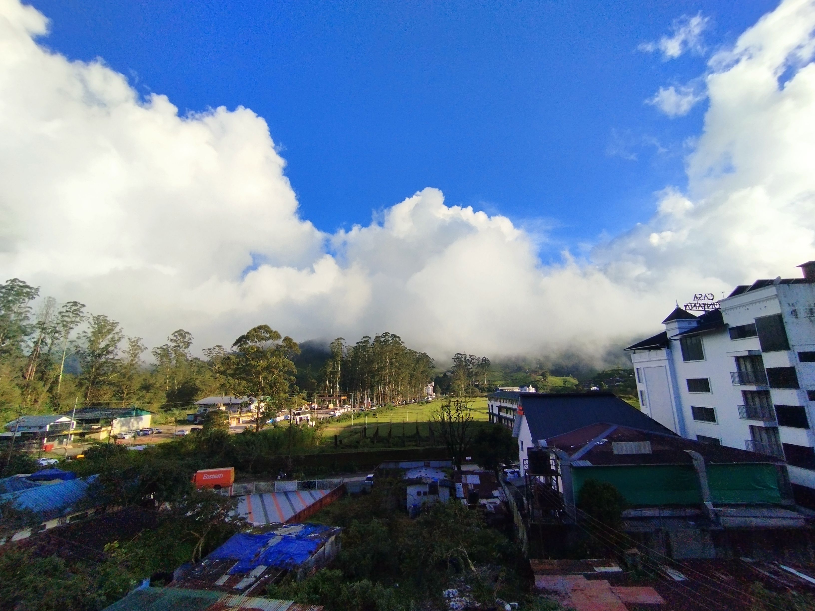 A residential area with houses, a large building with a sign, and a clear blue sky with clouds.