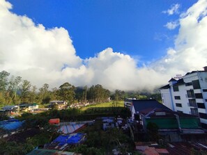 A residential area with houses, a large building with a sign, and a clear blue sky with clouds. - MSP Amma Cottage (Munnar)