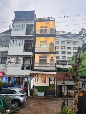 A multi-story building with a sign 'MDFAMMA' on the top floor, a visible entrance, and a staircase leading to the entrance. - MSP Amma Cottage (Munnar)