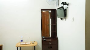 A room with a wooden cabinet, a television mounted on the wall, and a small table with a bottle and glasses.