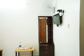 A room with a wooden cabinet, a television mounted on the wall, and a small table with a bottle and glasses. - MSP Amma Cottage (Munnar)