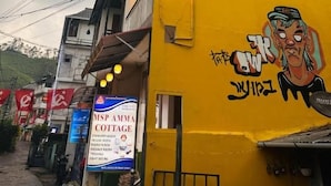 A multi-story building with a yellow facade, a visible sign for MSP AMMA COTTAGE, and a mural on the side.