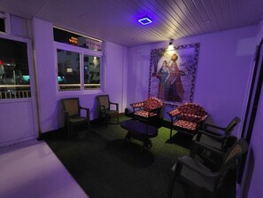 A room with a purple hue, featuring a table with chairs, a window with a neon sign, and a wall-mounted picture. - MSP Amma Cottage (Munnar)
