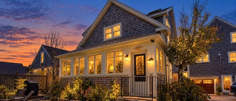 A two-story house with a stone foundation, a front porch, and a well-lit exterior.