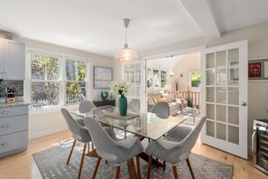 Een moderne eethoek met een glazen tafel, grijs gestoffeerde stoelen en een decoratieve vaas.