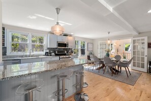 Een moderne keuken met een groot schiereiland, barkrukken en een eethoek met stoelen en een tafel.