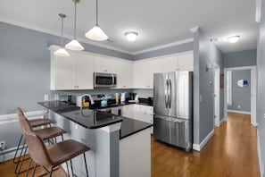 A modern kitchen with white cabinets, stainless steel appliances, and a central island with bar stools. - Marina View Townhome Overlooking Northwest Creek Marina (New Bern)