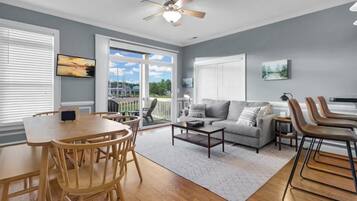 A living room with a grey sofa, a coffee table, and a dining area with a wooden table and chairs.
