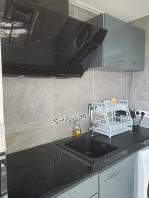 Una cocina con encimera negra, un lavabo y un escurreplatos.