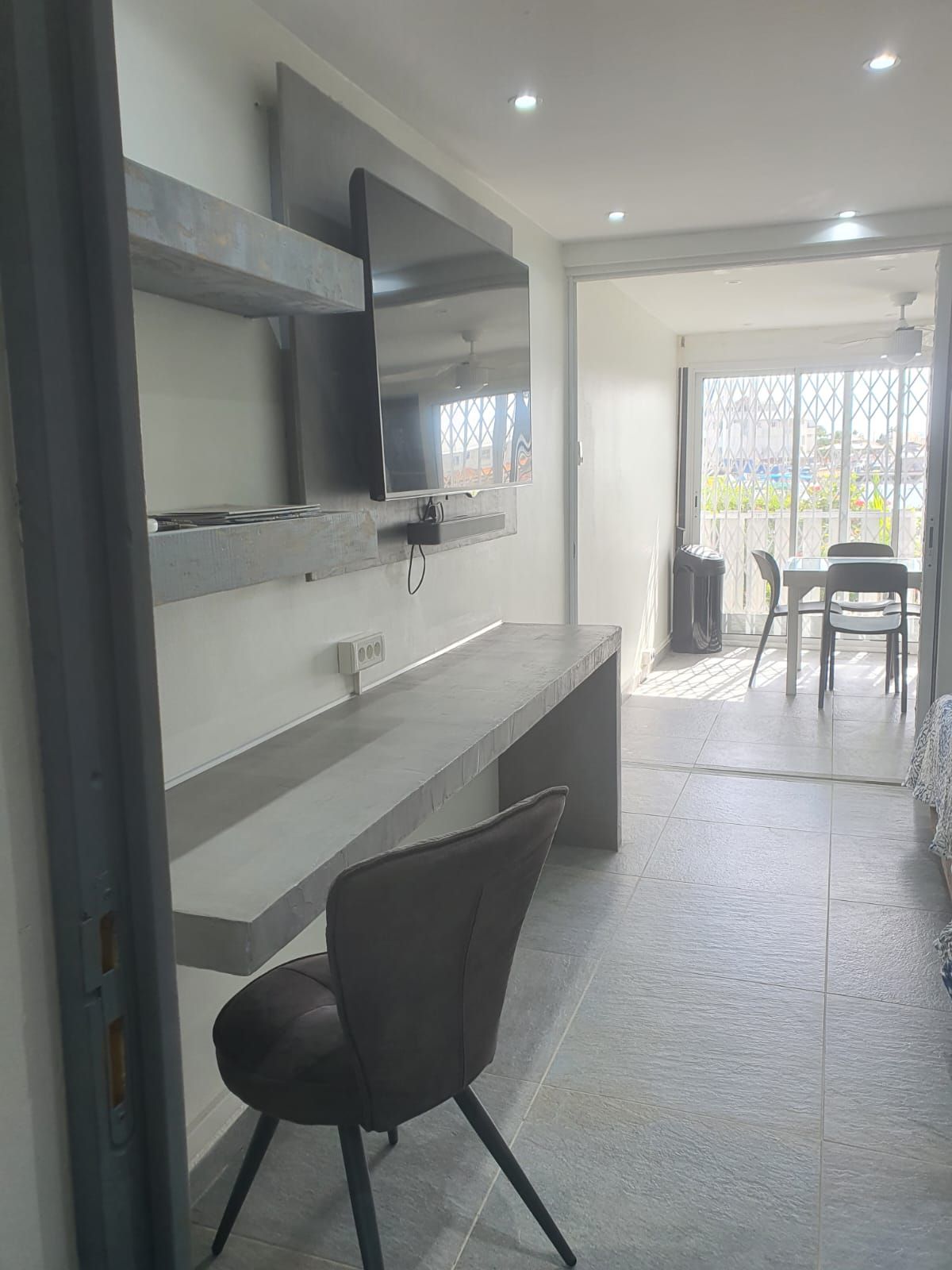 Un intérieur moderne avec un téléviseur à écran plat fixé au mur, un banc gris et un coin repas comprenant des chaises et une table.