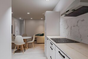 A modern kitchen with a built-in stove, white cabinetry, and a dining area with a round table and chairs. - Apartment 'Piso Martita' with Wi-Fi (Cedeira)
