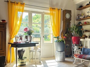 A room with a table, chairs, a clock, and potted plants. - Au Clair Ventoux (Saint-Didier)