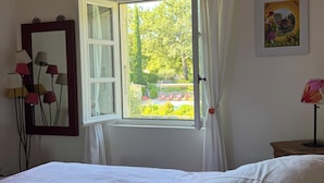 A bedroom with a bed, a window with curtains, a mirror, and a lamp.