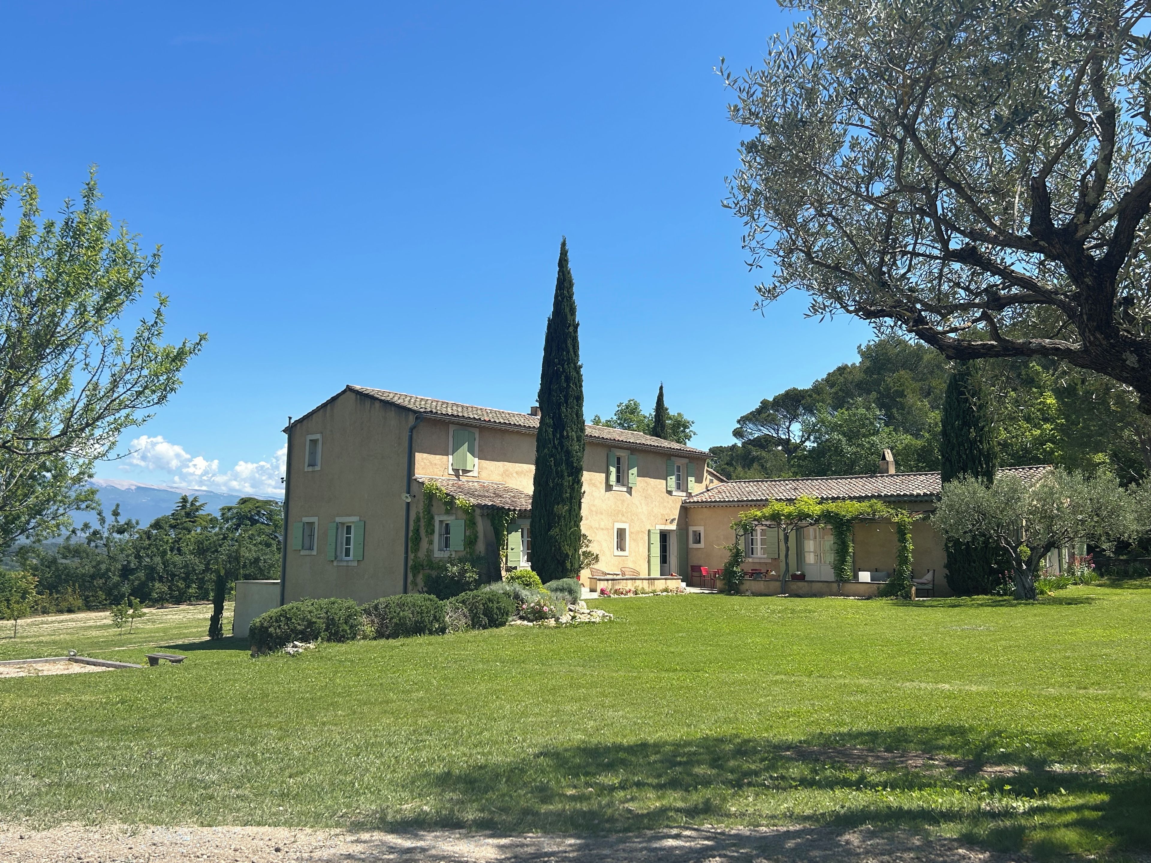A two-story building with a tiled roof, surrounded by a well-maintained lawn and mature trees.