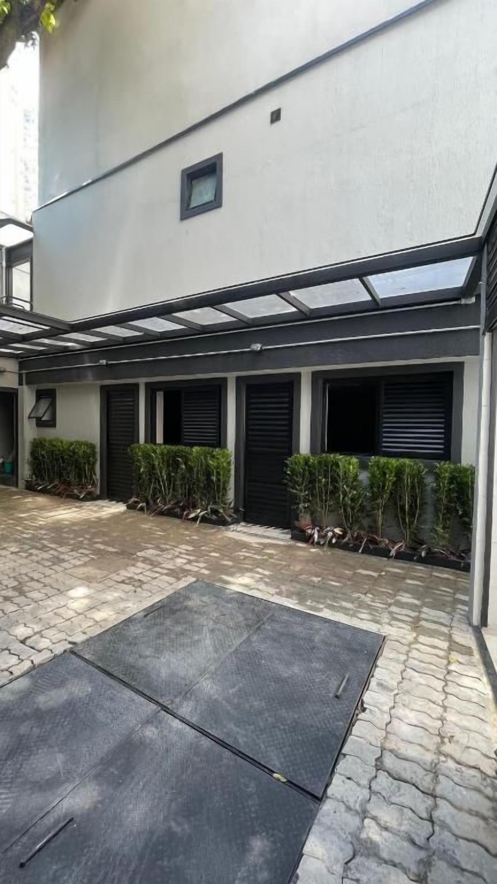 Un patio con suelo empedrado, una zona de estar techada y un edificio con varias ventanas y techo plano.
