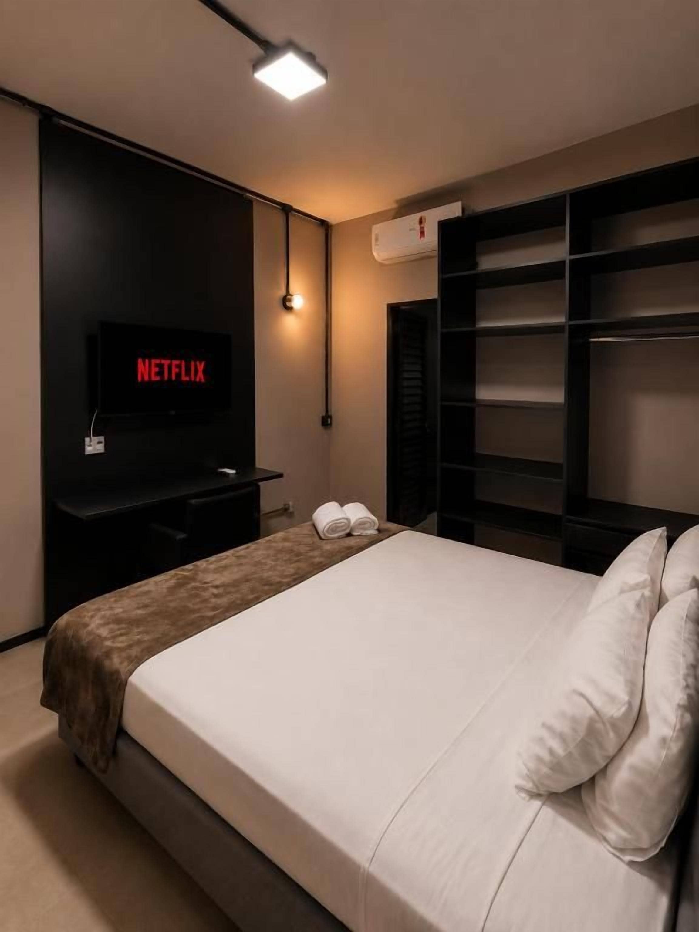 A hotel room with a bed, a TV mounted on the wall, a bedside table, and a wardrobe.