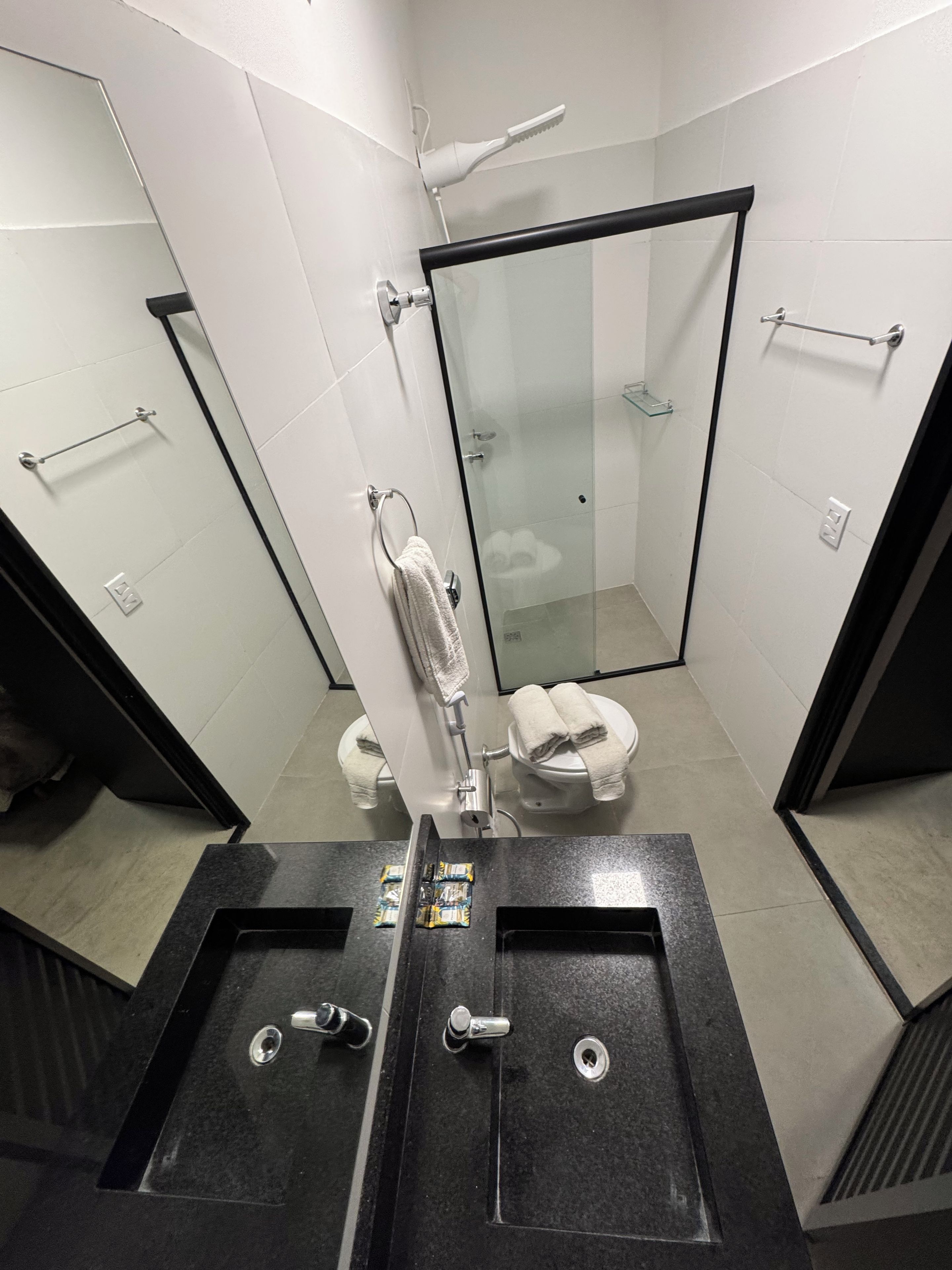 A modern bathroom with a glass shower enclosure, a toilet, and a sink with a towel rack.
