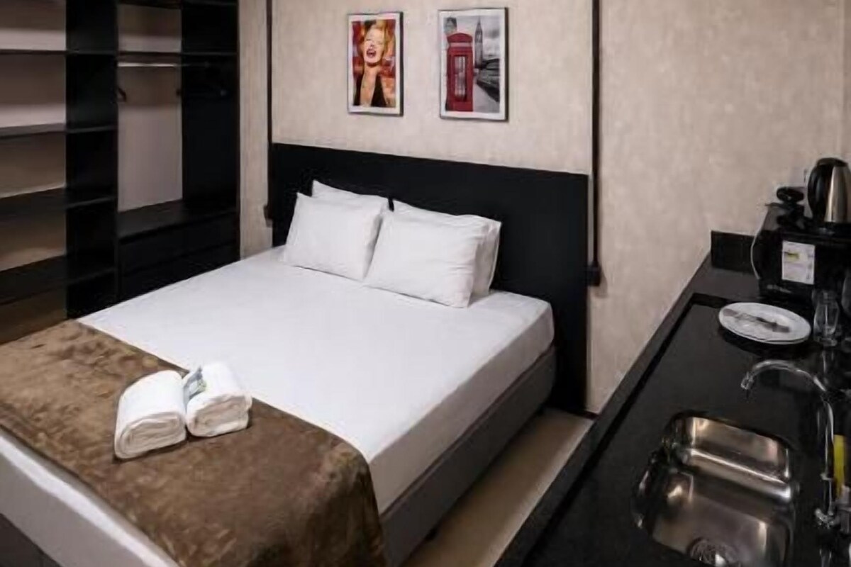 A hotel room with a bed, a small kitchenette, and a wall-mounted shelf.