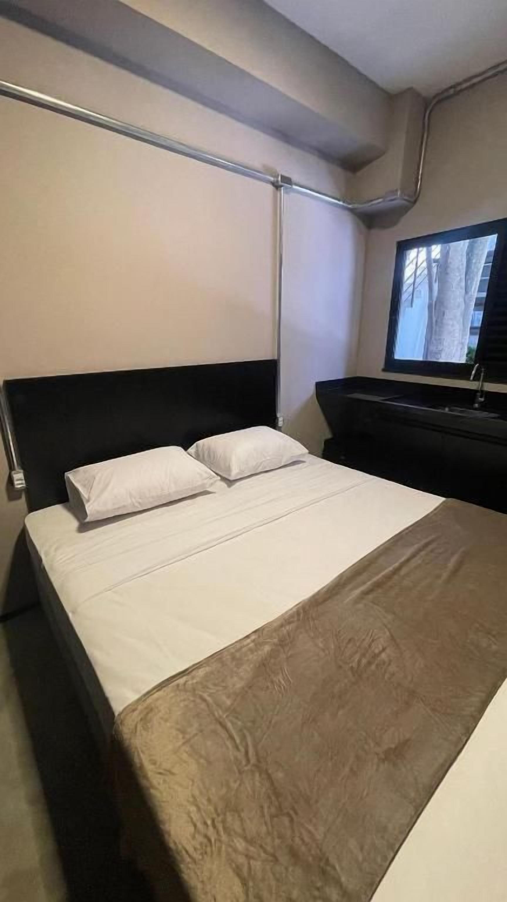 Una habitación de hotel con cama, escritorio, ventana y televisor de pared.
