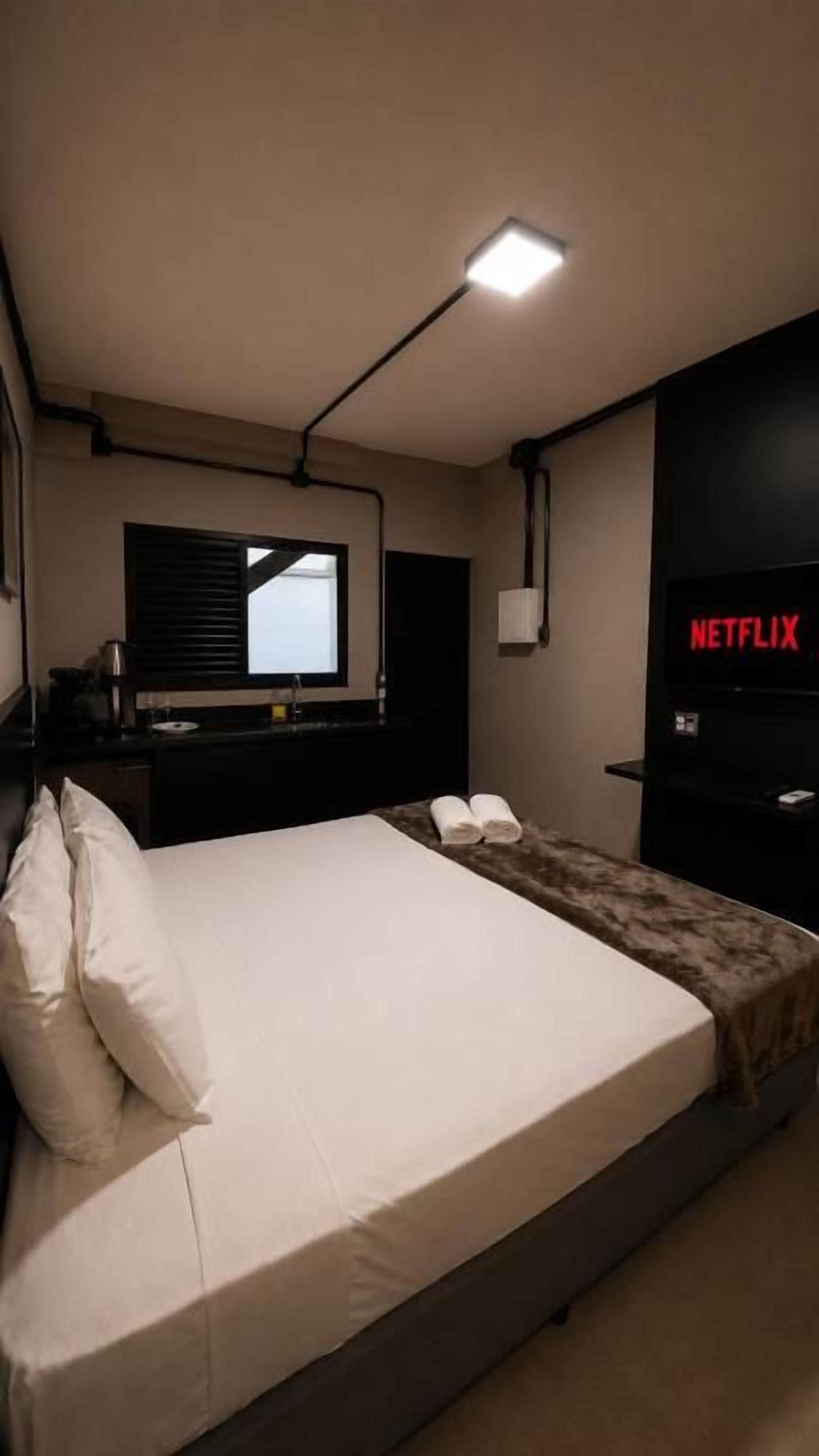 A bedroom with a bed, a TV, a desk, and a window.