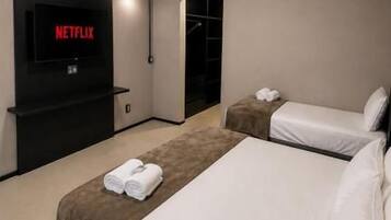 Una habitación de hotel moderna con una cama grande, un televisor mostrando 'NETFLIX' y un equipo de aire acondicionado montado en la pared.