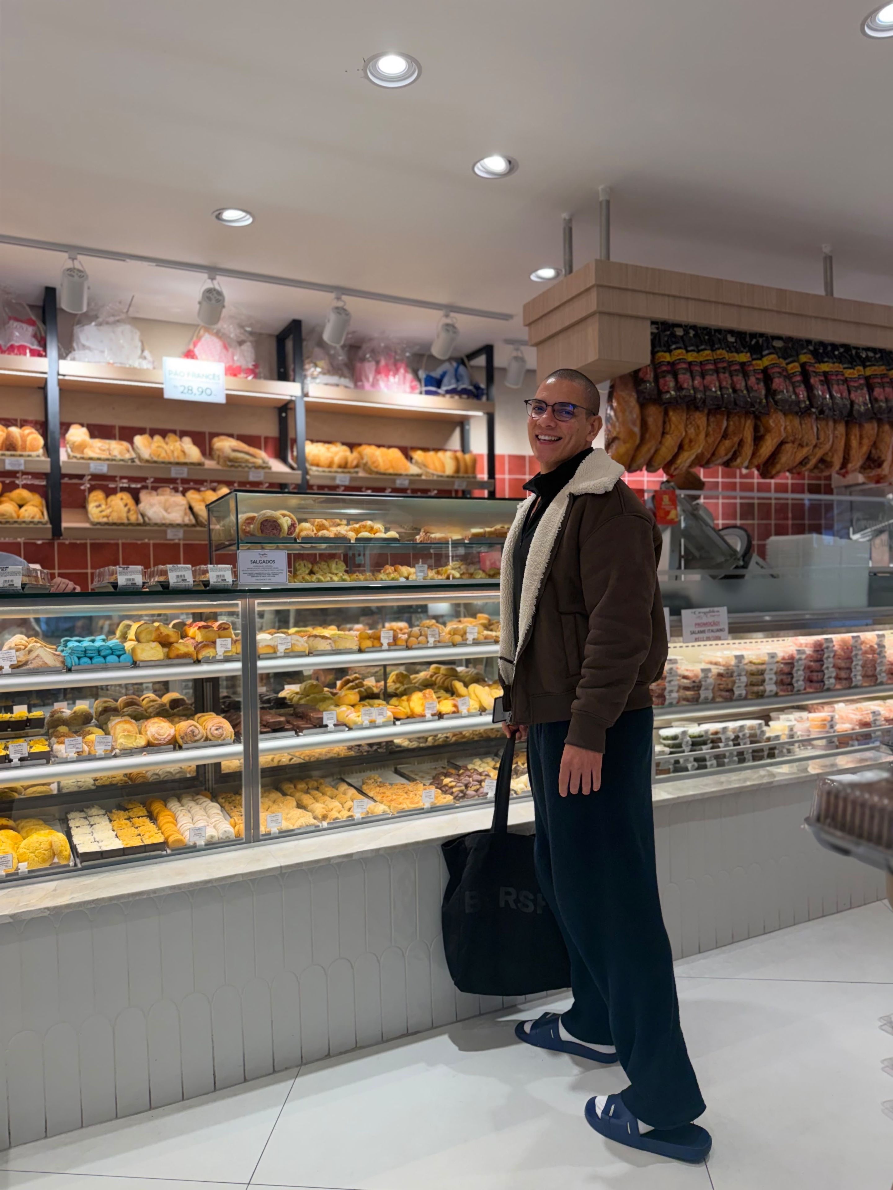 Une personne se tient devant une vitrine de boulangerie où sont exposés divers produits de pâtisserie.