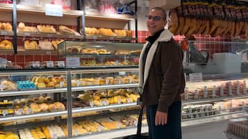 Une personne se tient devant une vitrine de boulangerie où sont exposés divers produits de pâtisserie.