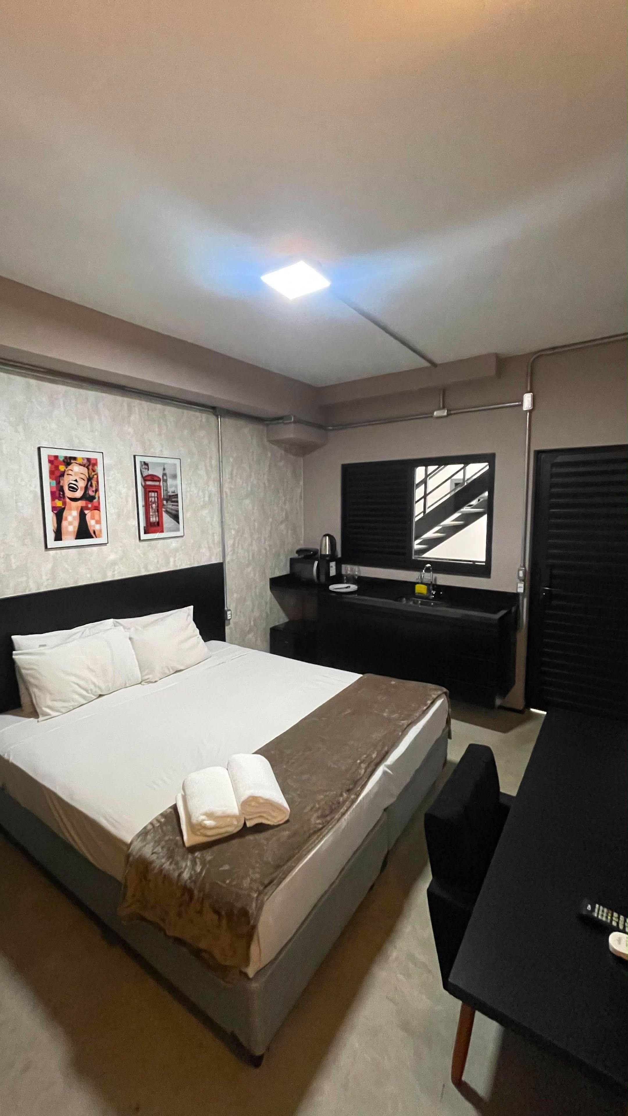 A hotel room with a bed, a desk, a mirror, a coffee machine, and artwork on the wall.